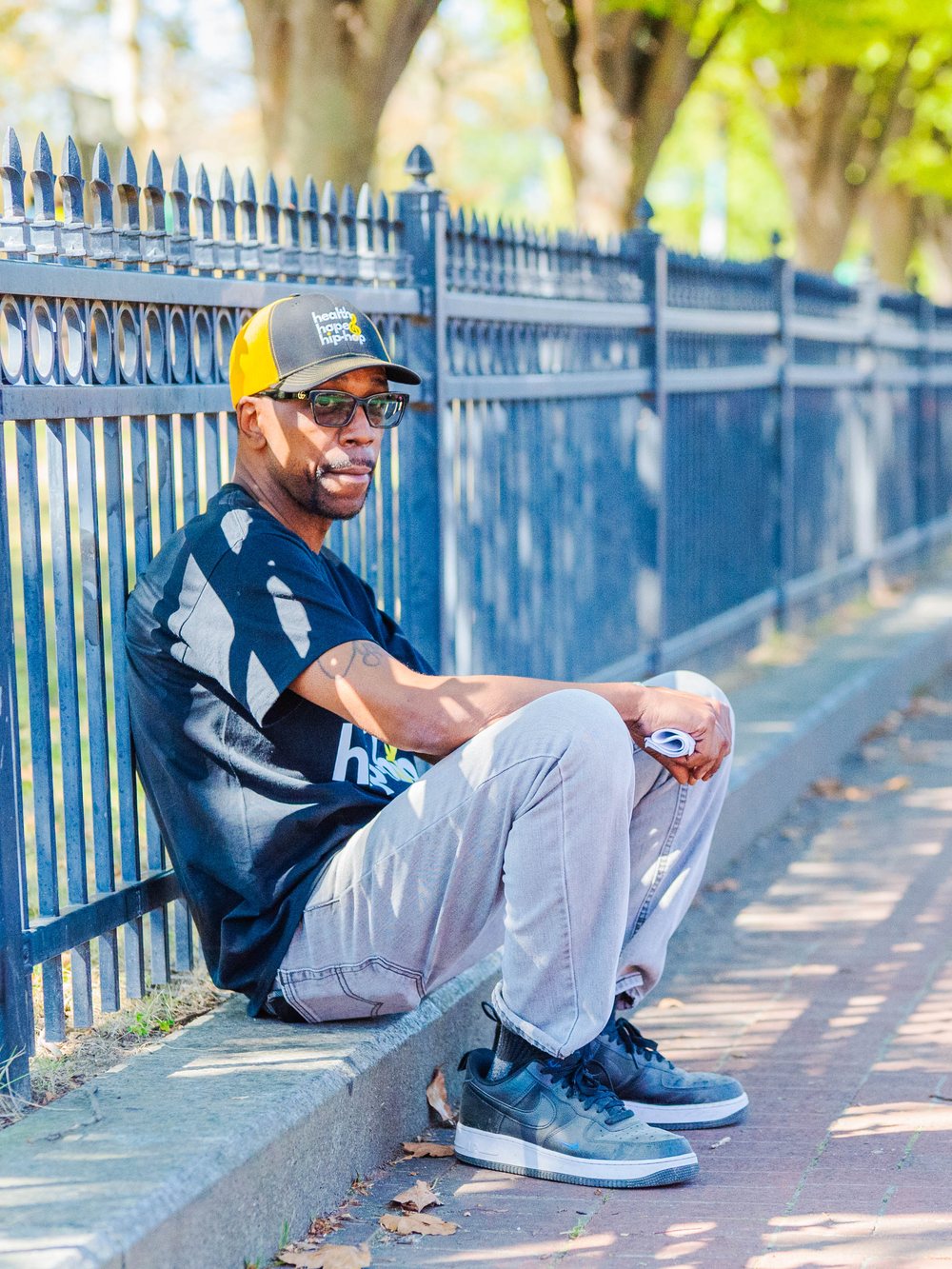 Oya Gilbert sitting on a curb in a Health, Hope and Hip-Hop cap and shirt.